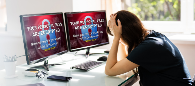 Distressed person sitting in front of two screens which are showing a ransomware attack.